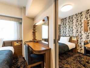 A hotel room with a desk, two beds, a mirror, a bedside table with a phone, and a wall with a floral pattern. - APA Hotel Tottori Ekimae (Tottori)