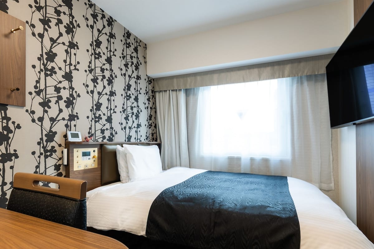 Ein Hotelzimmer mit einem Bett, einem Schreibtisch, einem Fernseher und einer Wand mit einem Blumenmuster.