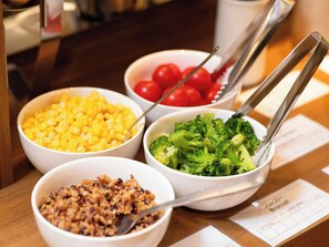 Una mesa con cuatro recipientes que contienen maíz, brócoli, tomates cherry y un plato de cereales.