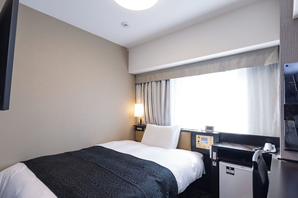 Una habitación de hotel con cama, escritorio, minibar y ventana con cortinas.