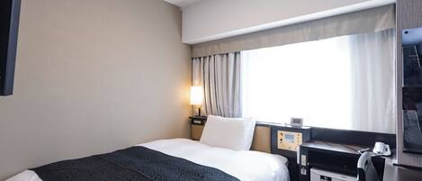 A hotel room with a bed, a desk, a minibar, and a window with curtains.