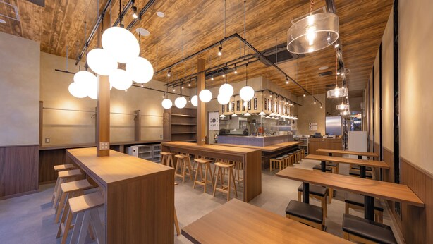 Un interior de restaurante moderno con mesas y taburetes de madera, lámparas colgantes y una zona de bar central.