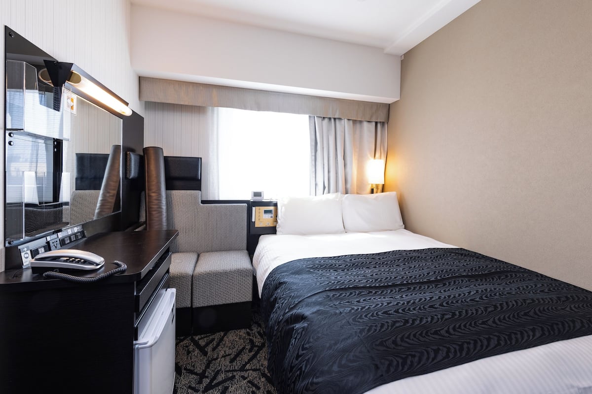 Habitación de hotel con cama, escritorio con teléfono, televisión y ventana con cortinas.