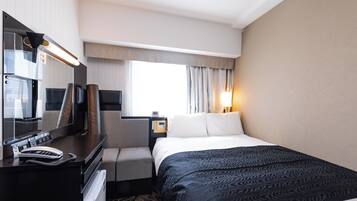 Habitación de hotel con cama, escritorio con teléfono, televisión y ventana con cortinas.