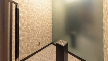 A corner of a room with patterned walls, a door, and a small trash bin.