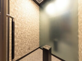 Esquina de una habitación con paredes estampadas, una puerta y un pequeño cubo de basura.