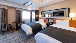 Habitación de hotel con dos camas, un escritorio, una silla, un espejo grande y una lámpara en el techo.