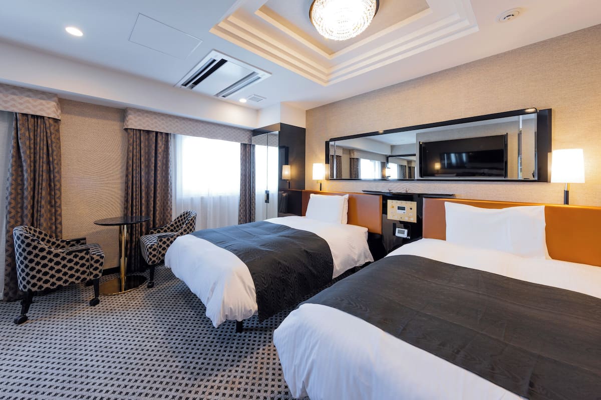 Habitación de hotel con dos camas, un escritorio, una silla, un espejo grande y una lámpara en el techo.