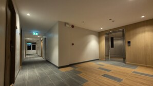 A hotel corridor with a tiled floor, wooden paneling on the walls, an elevator, and a fire alarm. - The Publyc Hotel (Bangkok)