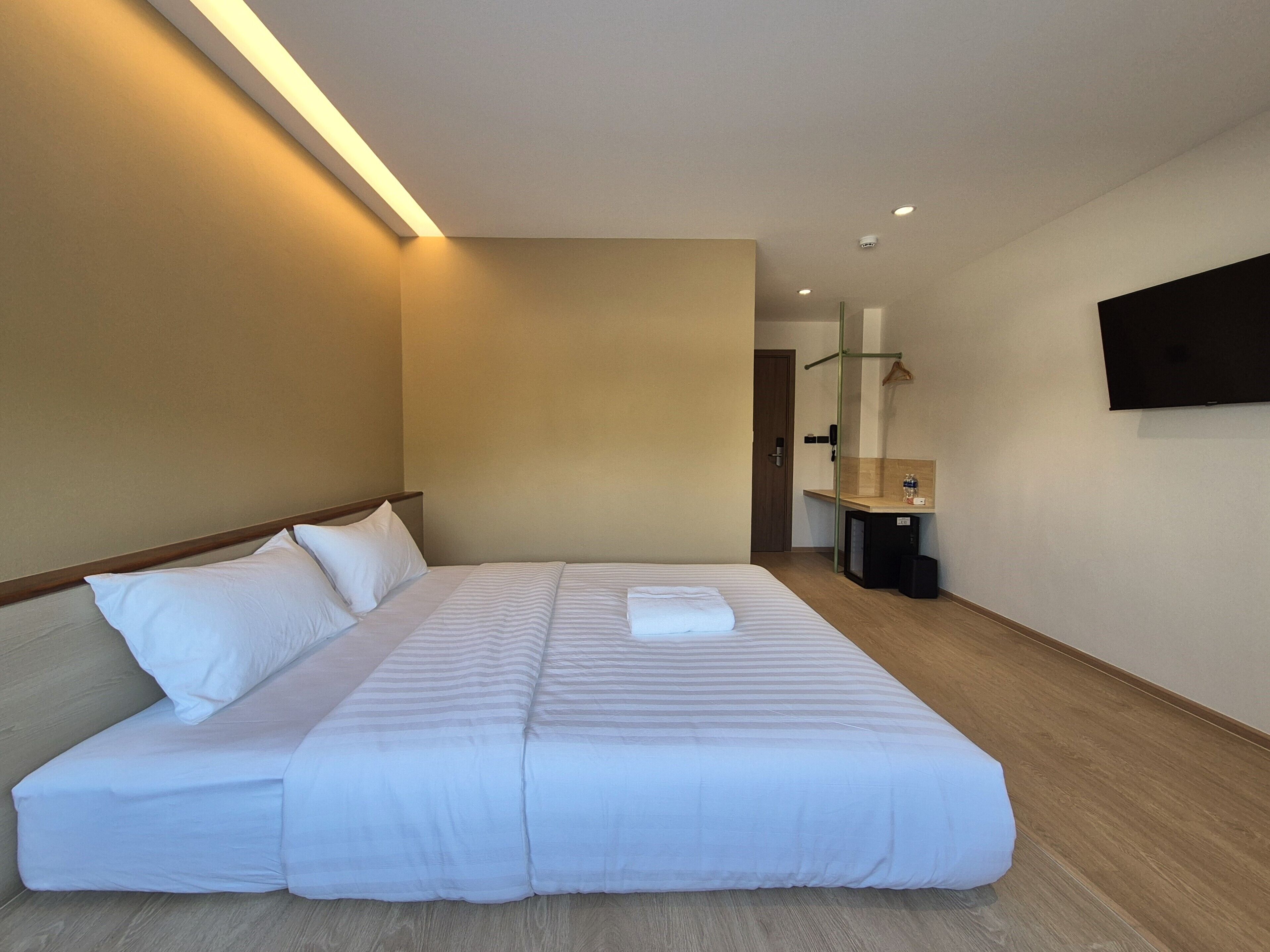 A neatly made bed with white linens, a bedside table with a mirror, and a flat-screen TV mounted on the wall.