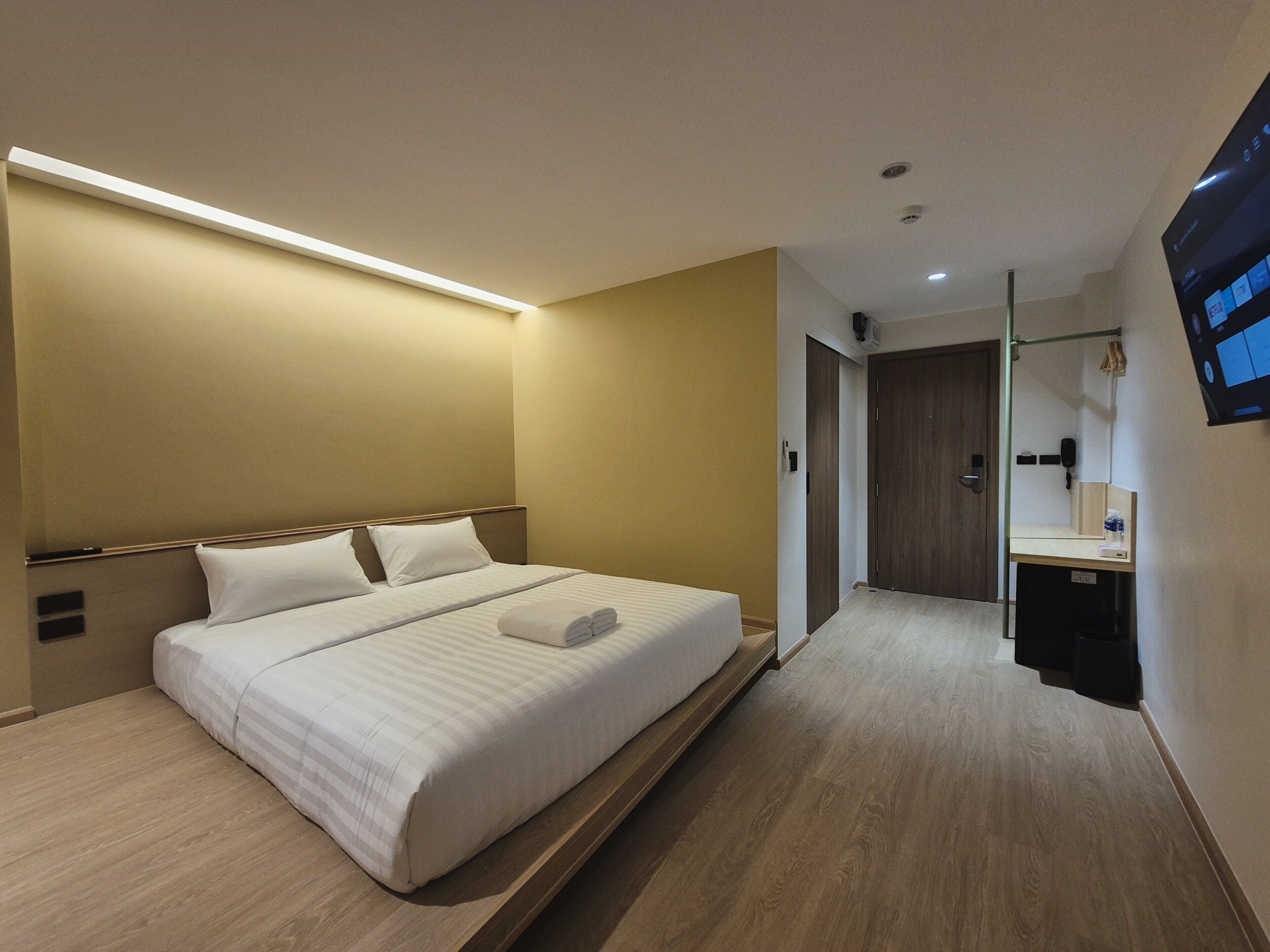 A modern hotel room with a large bed, bedside tables, a built-in desk, and a mirror.