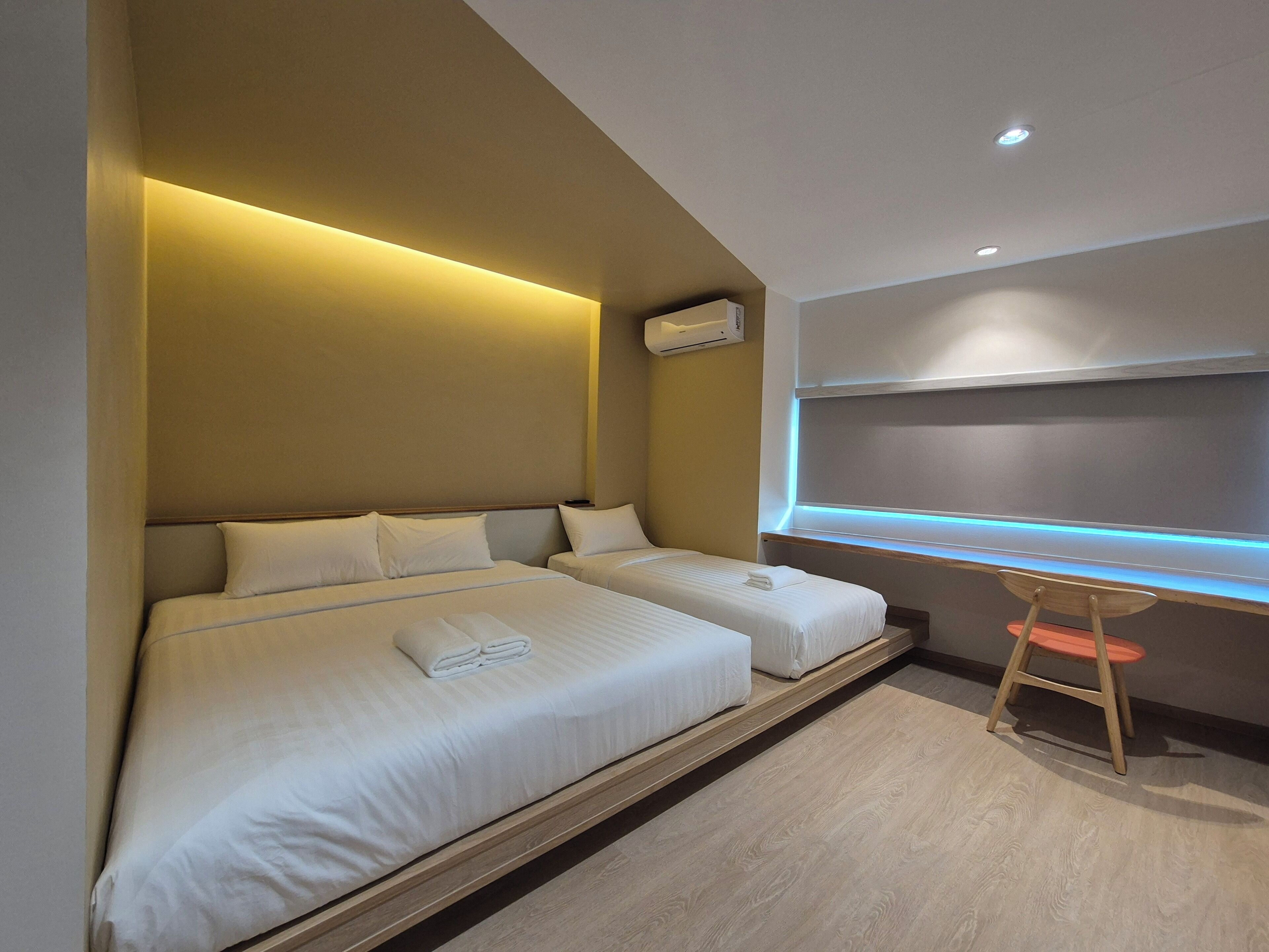 A modern hotel room with two beds, a desk, and a window with blue LED lighting.