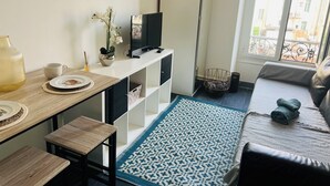 Un salon moderne avec un canapé, une table basse, un téléviseur et une vue sur la ville grâce à de grandes fenêtres.