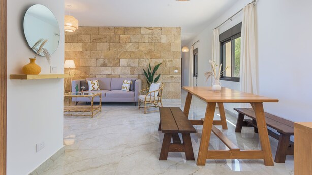 A modern living room with a stone wall, a sofa, a dining table with benches, and a hanging light fixture.
