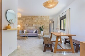 A modern living room with a stone wall, a sofa, a dining table with benches, and a hanging light fixture. - Glow Studios & Apartments in Batroun  (Batroun)