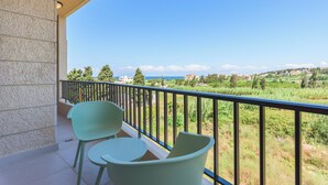 A balcony with two chairs and a table, overlooking a scenic landscape with buildings and greenery.