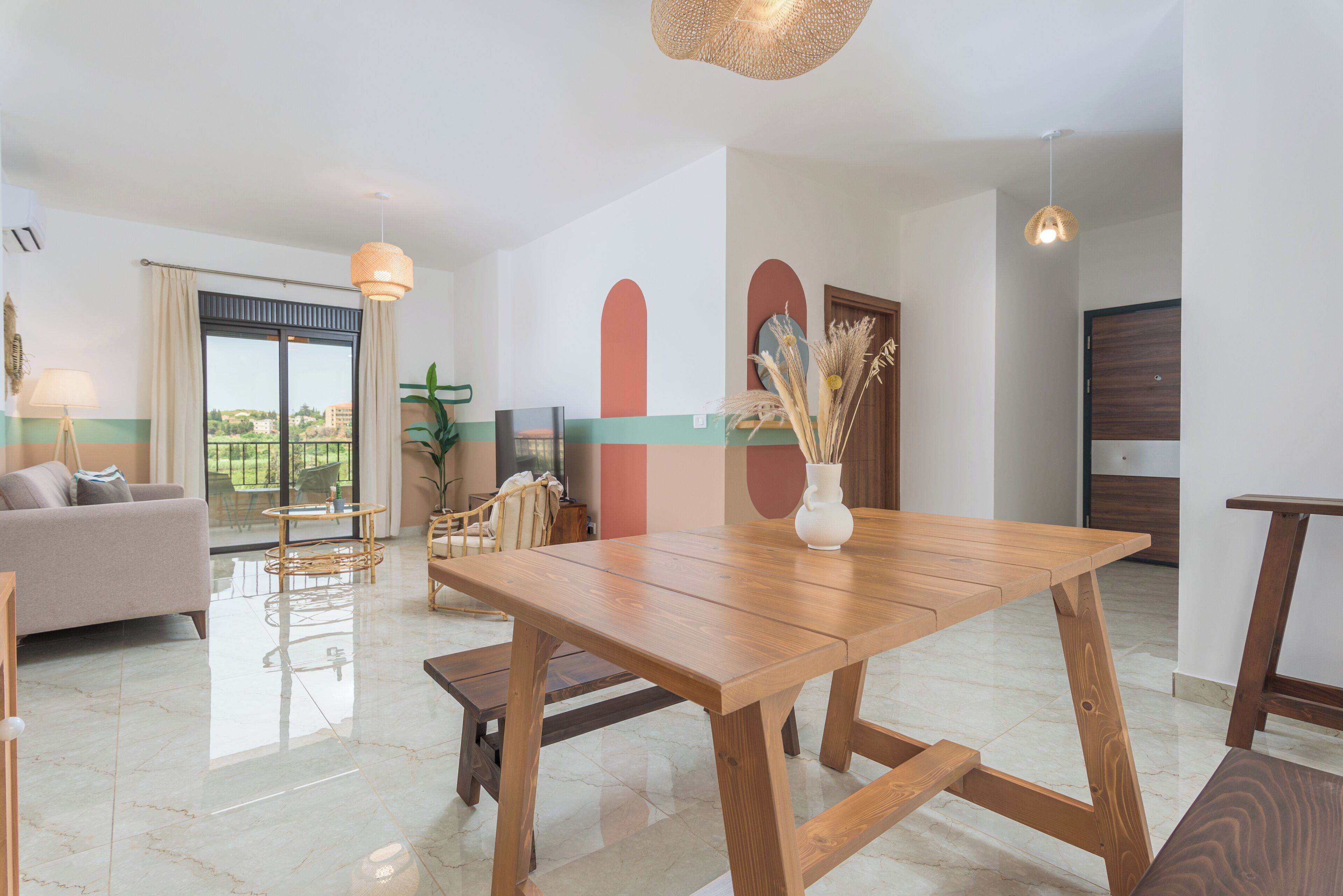 A modern living room with a wooden dining table, a sofa, and a large window offering a view of the outdoors.