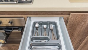 A drawer with utensils including spoons, a fork, and a bottle opener.