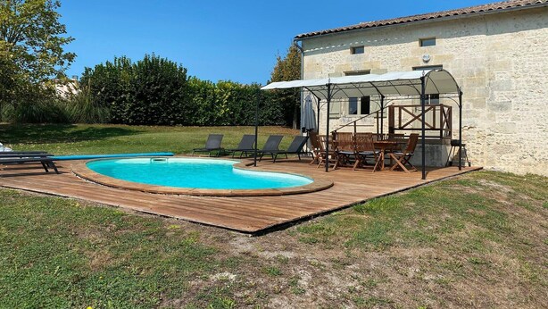 A swimming pool with a wooden deck, lounge chairs, and a covered patio area.