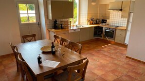 A compact kitchen with a dining area, featuring a wooden table, chairs, a built-in oven, and a window providing natural light.