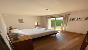 A bedroom with a large bed, a bedside table, a nightstand, a window with curtains, and a view of greenery outside. - Charming Home in Dordogne near Vineyards (Chalais)
