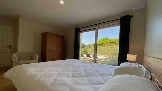 Une chambre avec un grand lit, une armoire en bois, une chaise et une vue sur l’extérieur grâce à une porte coulissante.