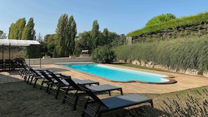 Une piscine avec des chaises longues, un espace salon couvert et une terrasse en bois.