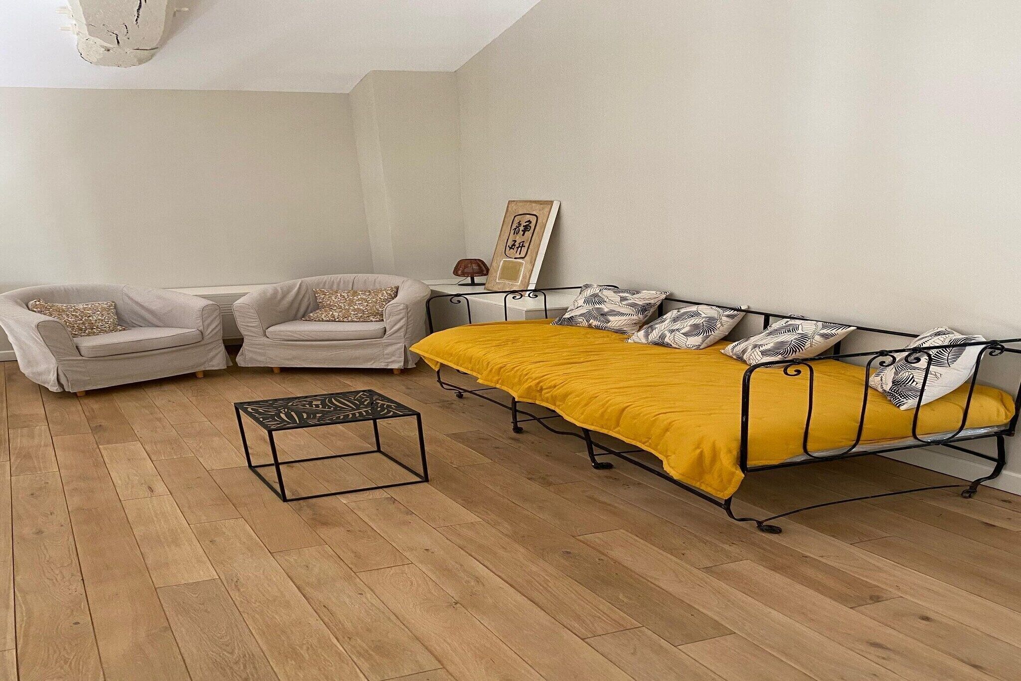 Een kamer met een bed, twee fauteuils, een bijzettafeltje en een wandplank.