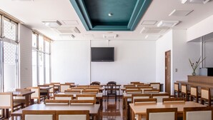 Ein Klassenzimmer mit Holztischen und -stühlen, einem großen Flachbildfernseher an der Wand und einer Decke mit Einbaustrahlern.