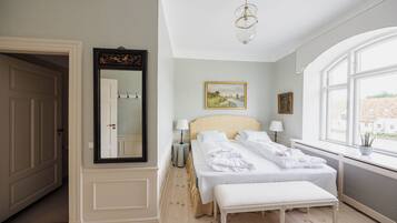 Habitación de hotel con una cama grande, un banco, un espejo y una ventana con vista a edificios.