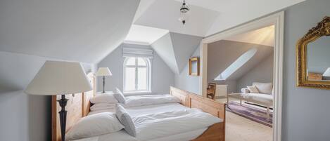 Quarto com cama de madeira, roupa de cama branca, mesa de cabeceira com abajur, janela e espelho na parede.