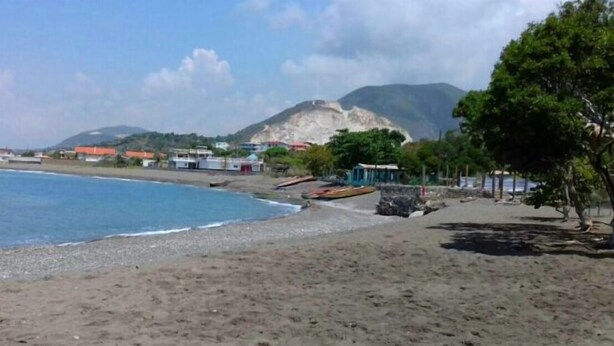 A beach with a clear view of the sea, a sandy shore, and a mountain in the background.