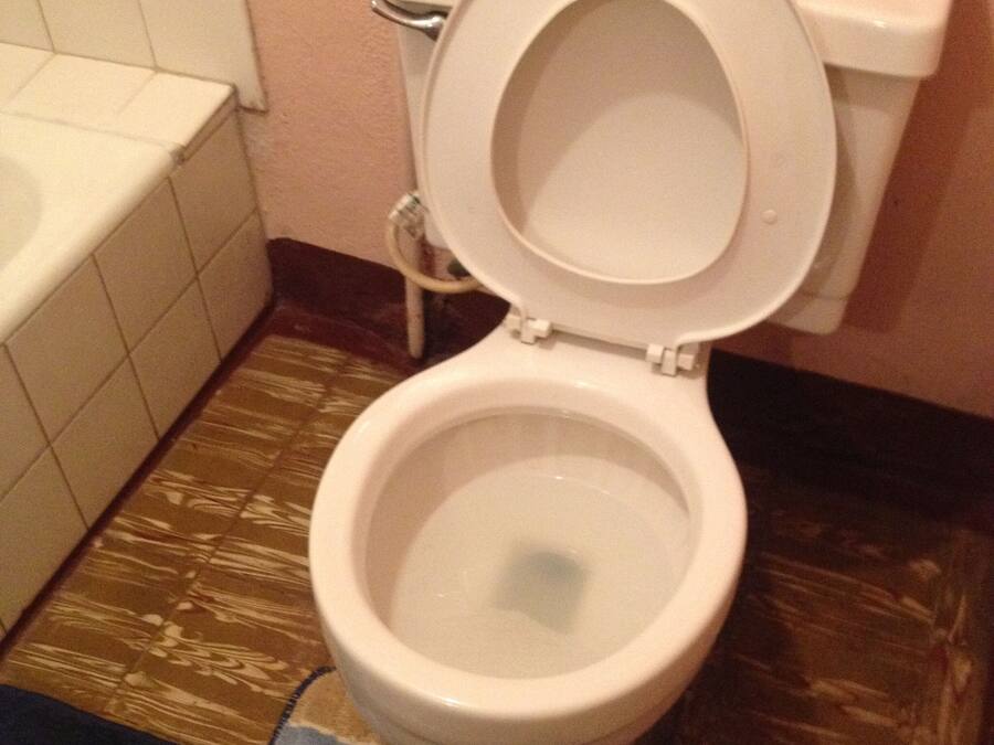 Eine weiße Toilette mit geschlossenem Deckel, eine weiße Badewanne und ein gefliesteter Boden.