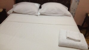 A neatly made bed with white linens and pillows, a folded white towel, and a dark headboard.