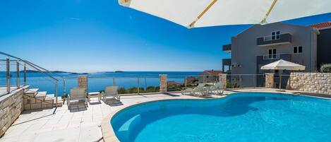 Una piscina con vistas al mar, mobiliario exterior y un edificio con balcones.