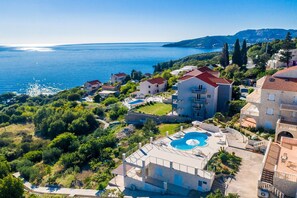 Un quartier résidentiel situé sur la côte, avec un grand immeuble doté d’une piscine, entouré d’une végétation luxuriante et offrant une vue sur la mer.