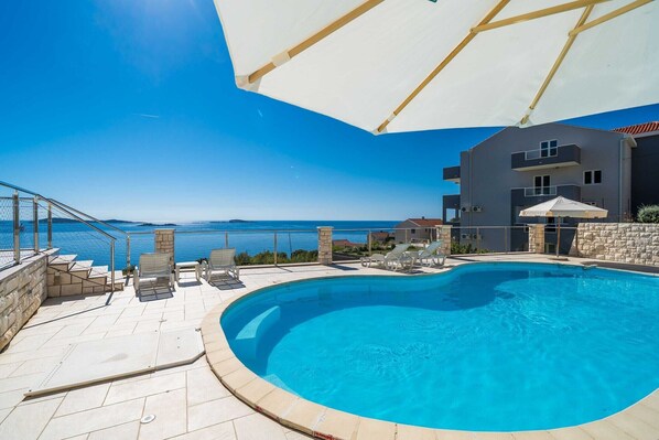 Une piscine avec vue sur la mer, un espace extérieur aménagé pour s’asseoir et un bâtiment doté de balcons.