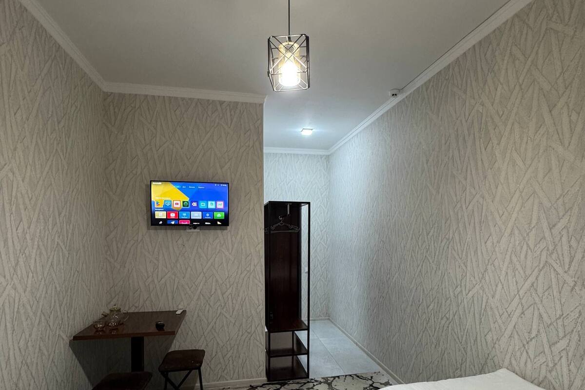 A hotel room with two beds, a desk with a chair, a TV mounted on the wall, and a patterned rug.