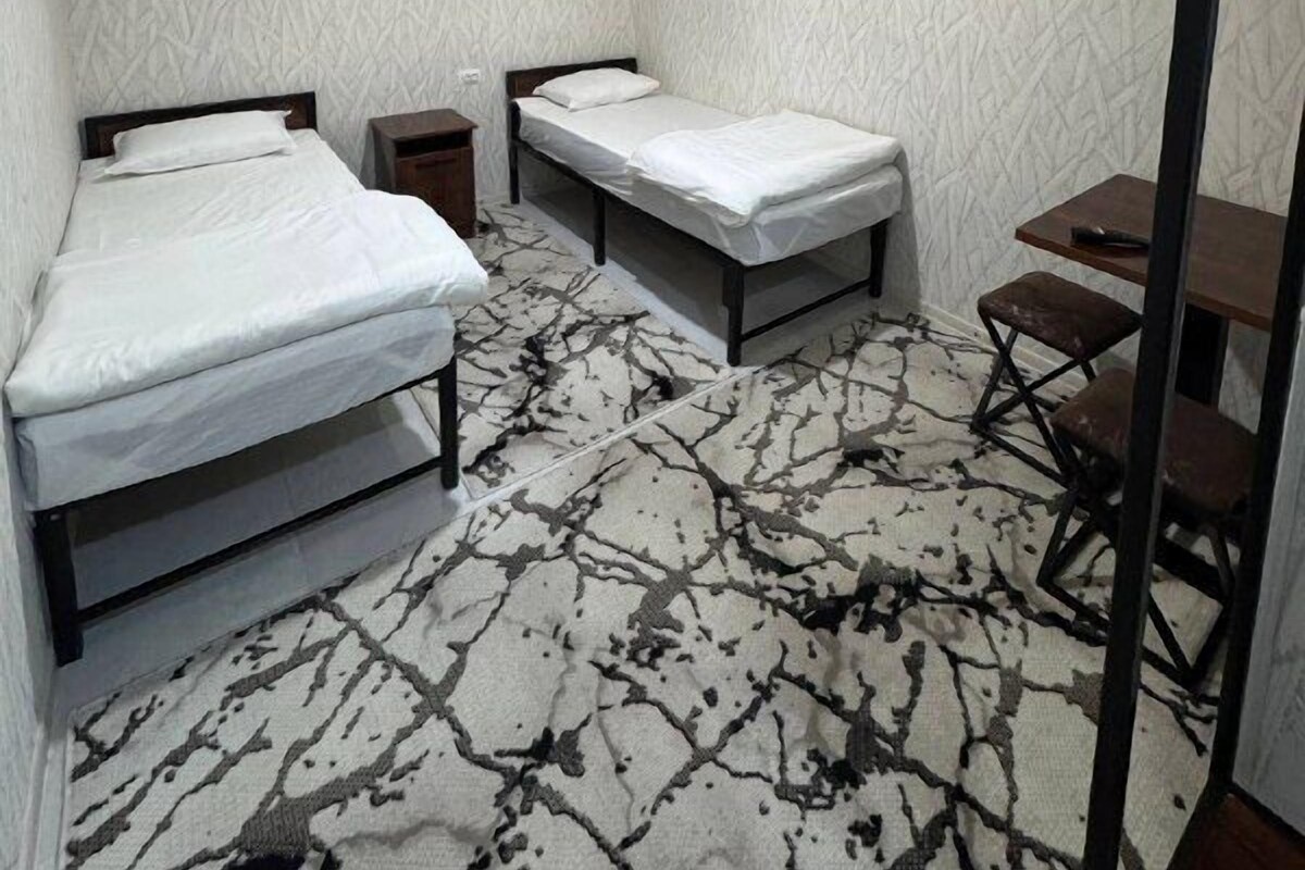 A small, compact room with two single beds, a small table, and a chair.