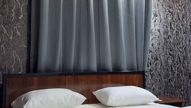 Ein Hotelzimmer mit Bett, grauen Vorhängen und einer strukturierten Wand.