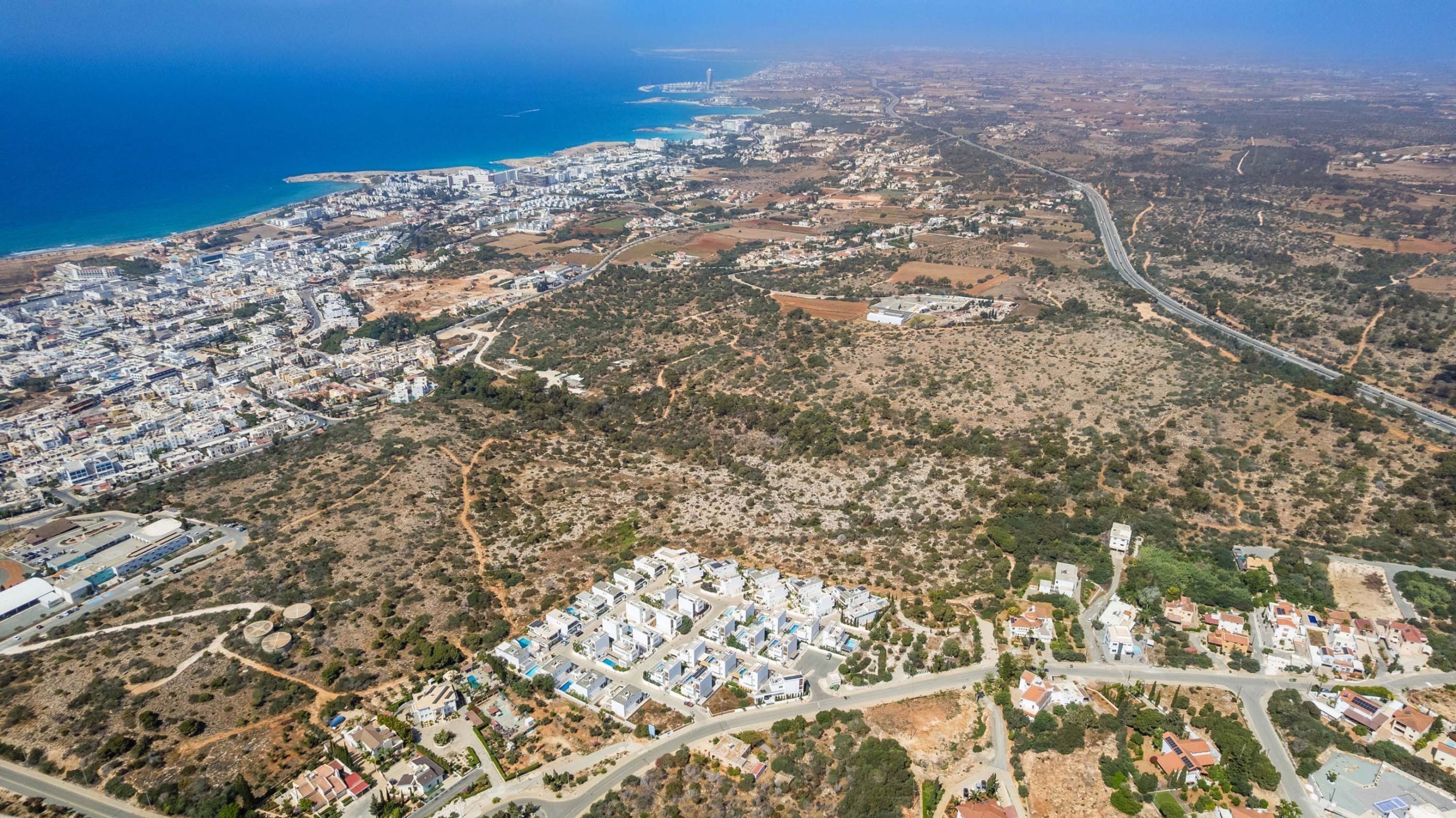 Vue aérienne d’une ville côtière avec des zones urbaines densément peuplées, un grand complexe résidentiel et une autoroute.