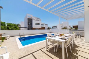 A rooftop pool with a white pergola, a dining area with white furniture, and a view of modern buildings in the background. - Elite Blu Heights Villa (Ayia Napa)