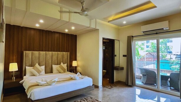 A modern bedroom with a large bed, a ceiling fan, and a view of the outside through a sliding glass door. - PAS RESORTS (Anjuna)