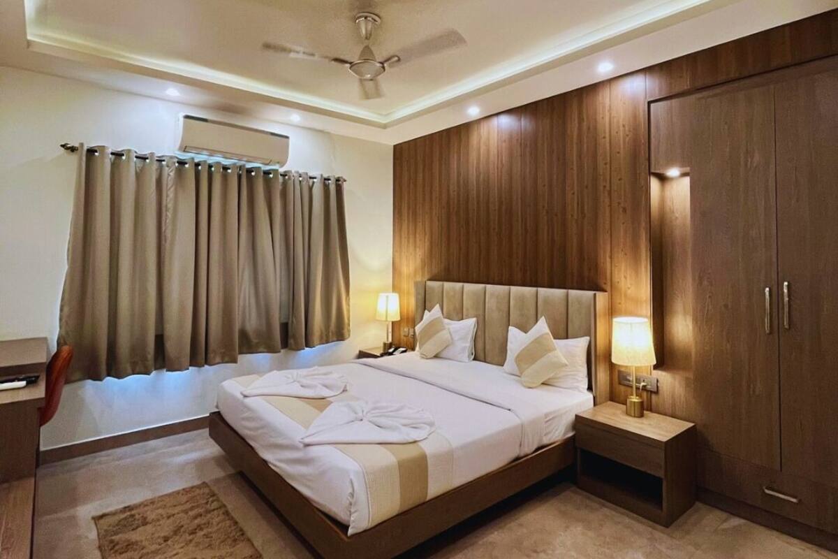 A modern hotel room with a large bed, wooden paneling, a ceiling fan, and a nightstand with a lamp.