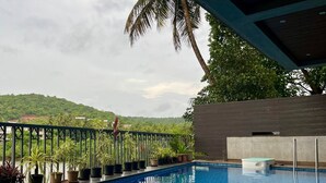 A swimming pool with a clear view of the surrounding landscape, including a hill and palm trees. - PAS RESORTS (Anjuna)