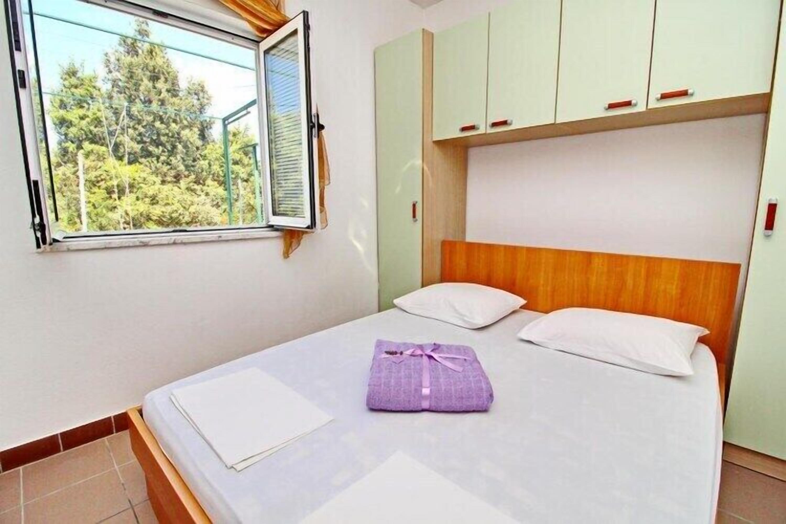 Una cama individual con cabecera de madera, una ventana con persianas y vistas a árboles.