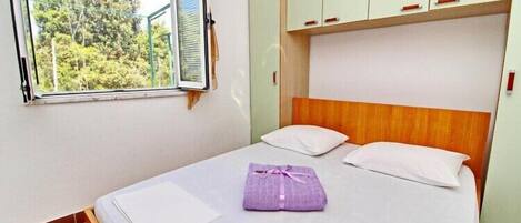 Una cama individual con cabecera de madera, una ventana con persianas y vistas a árboles.