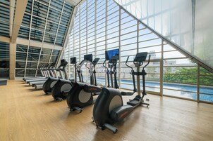 Un gimnasio con equipo de cardio y un amplio ventanal con vista a una piscina.