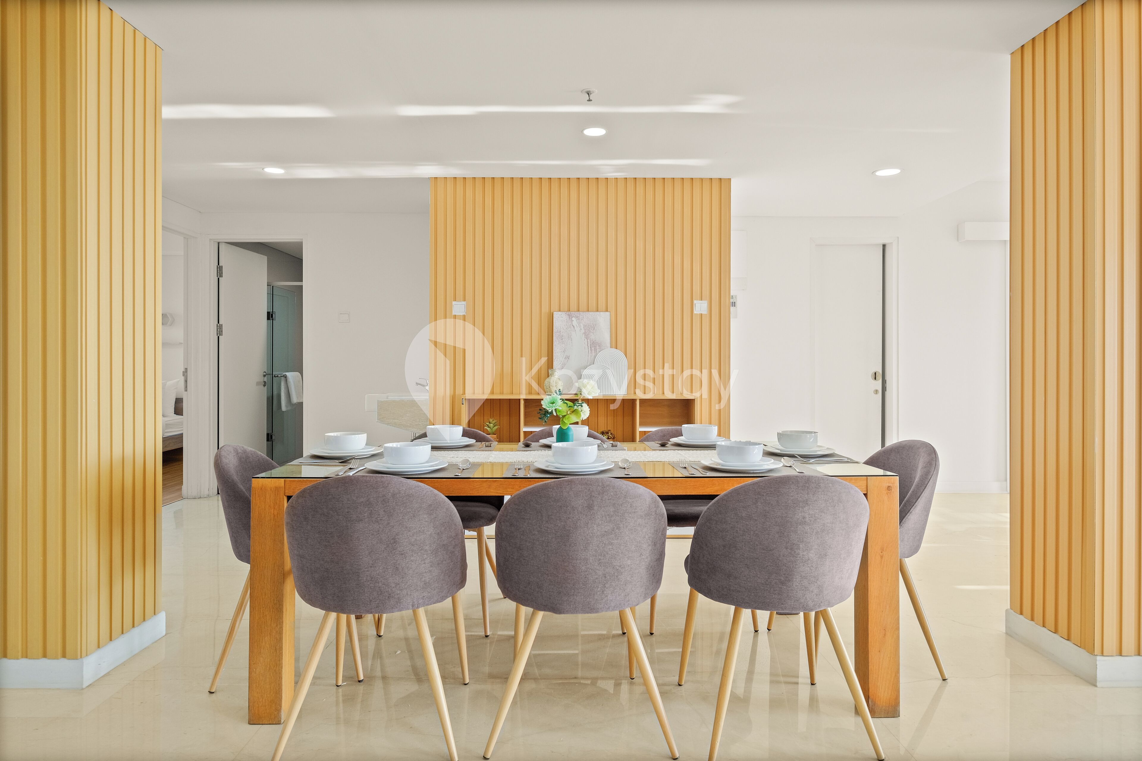 A modern dining area with a wooden table, six grey chairs, and a decorative wall panel.