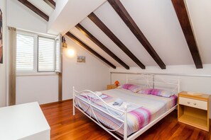 Ein Schlafzimmer mit schrägemausertem Dach, einem Bett mit weißem Metallgestell, einem Nachttisch und einem Beistelltisch.